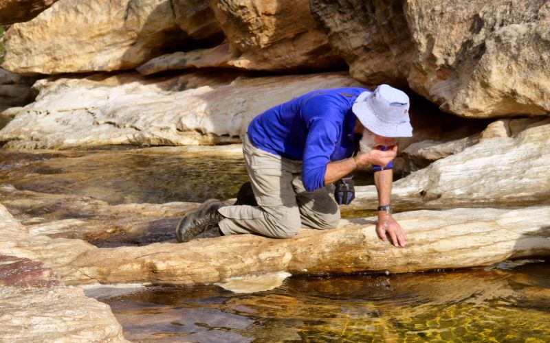 eco-cabins-senior-hiker-drinks-water-from-mountain-river-min